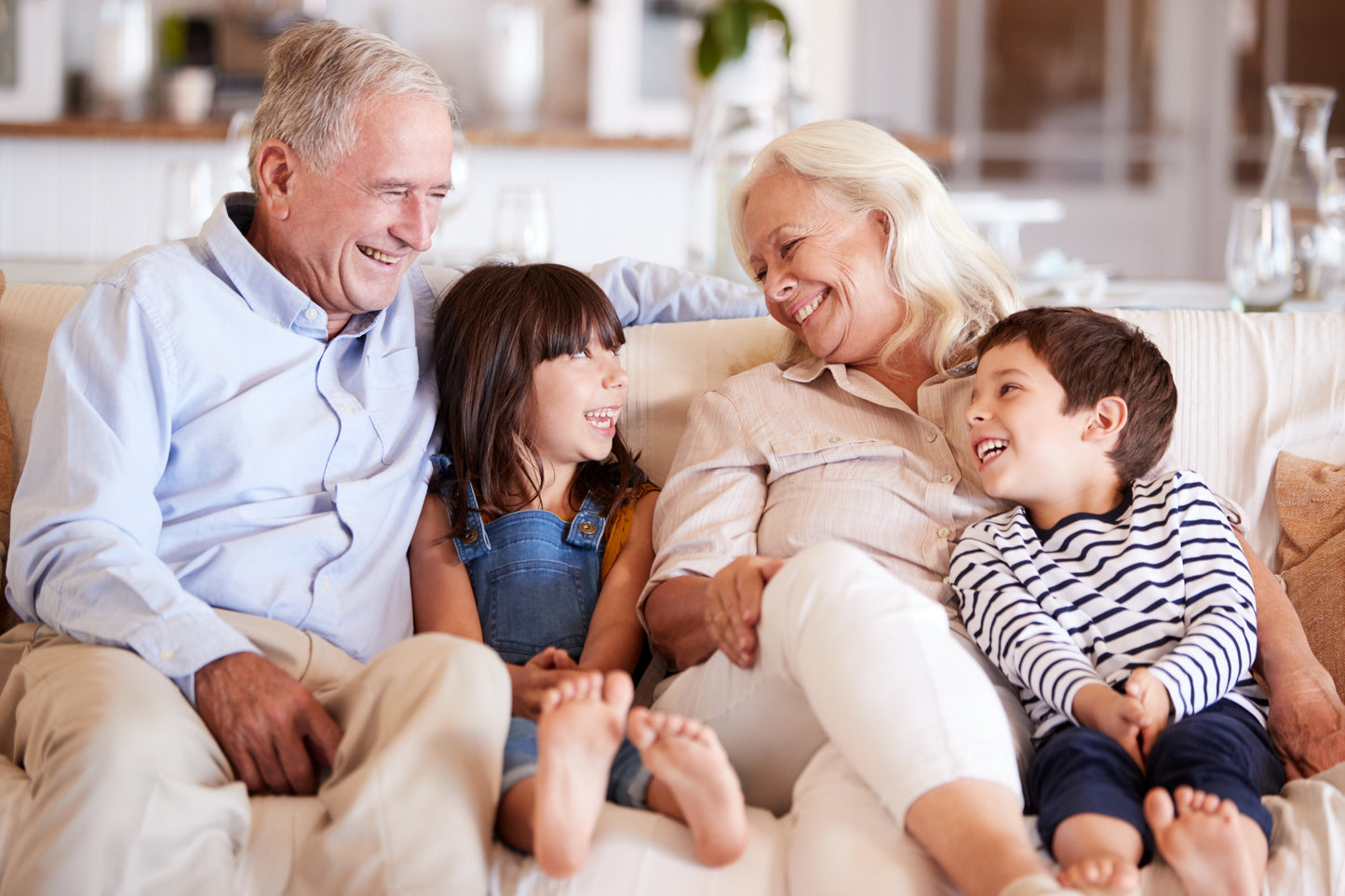 Grandfather and Grandmother sitting on a sofa with a granddaughter and grandson. All are enjoying a moment of happiness and connection. 